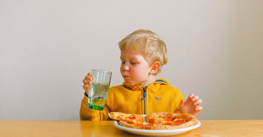 A cute blond child happily drinks while enjoying a pizza meal indoors.
